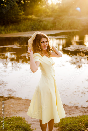 Young attractive girl with dark hair in a yellow summer dress by the river in summer at sunset. Healthy life.