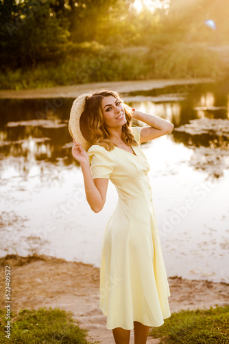 Young attractive girl with dark hair in a yellow summer dress by the river in summer at sunset. Healthy life.