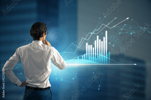 Back view of young european man looking at abstract glowing polygonal business graph hologram with growing arrow on blurry city background. Financial growth, market and trade concept.
