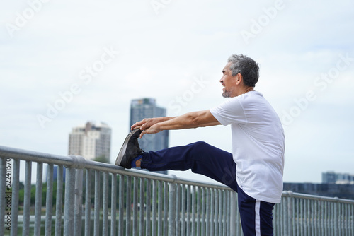 happy senior man with grey hair stretching legs in the city park, an old man warming up before workout to prevent injury. concept for elderly people lifestyle, health care, wellbeing