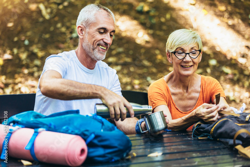 Mature couple sitting and drink coffee while resting in the forest after hiking.