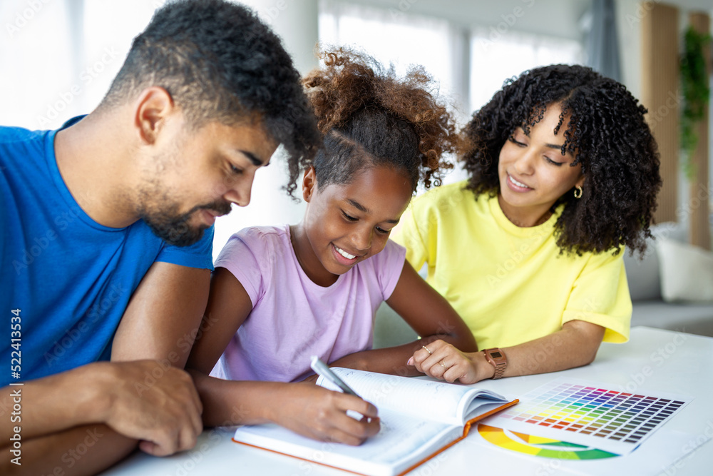 Front view of African American parents helping their daughter with homework at table, Photo of a young girl being homeschooled by her parents Front view of African American parents helping their daughter with homework at table, Photo of a young girl being homeschooled by her parents