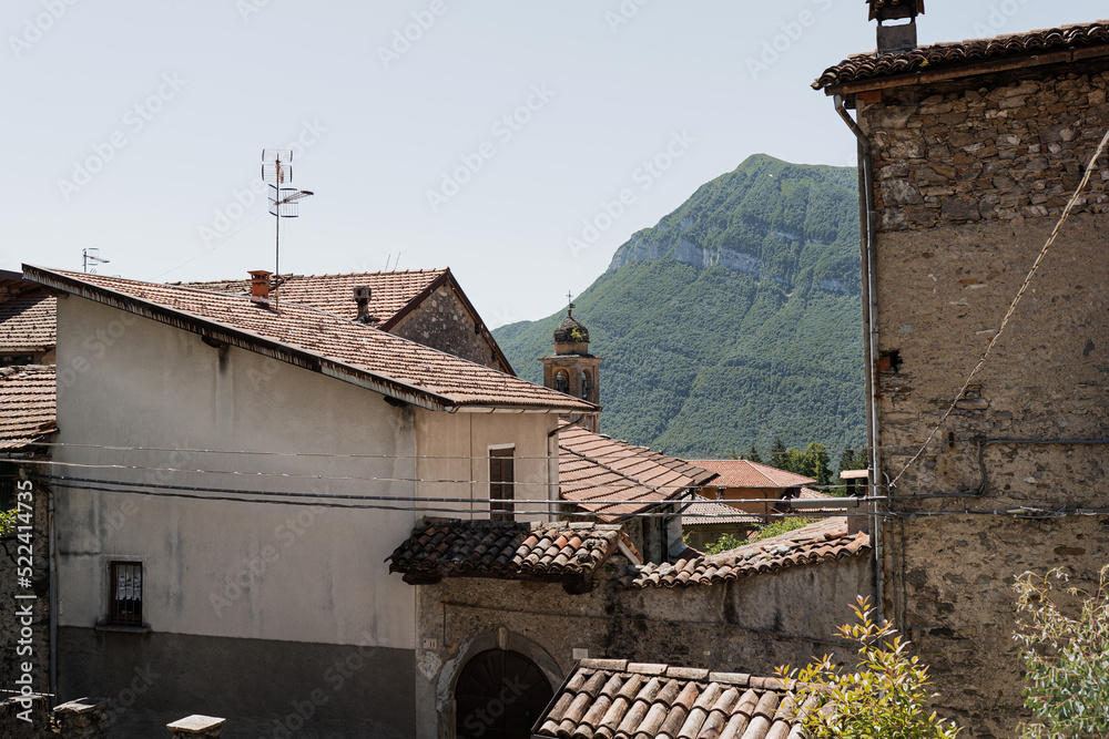 Obraz premium Rustic Italian architecture. Italian village in mountains with traditional buildings, wooden windows, flowers and blooming trees. Aesthetic summer vacation travel concept