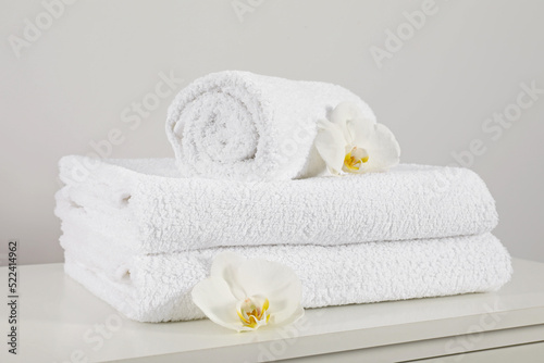 Clean soft white towels with flowers on table against light grey background