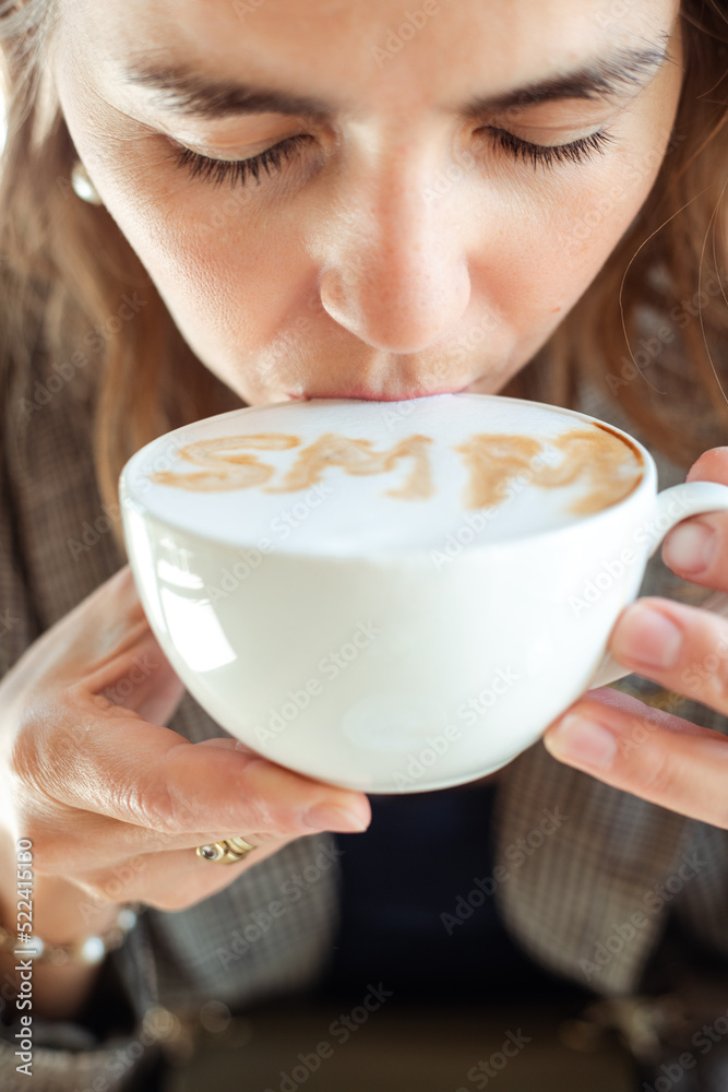 Young business woman drink hot flavored coffee with white foam with pleasure and closed eyes closeup. Social media marketing, SMM, promotion, delicious drinks in coffee house, meal time Young business woman drink hot flavored coffee with white foam with pleasure and closed eyes closeup. Social media marketing, SMM, promotion, delicious drinks in coffee house, meal time