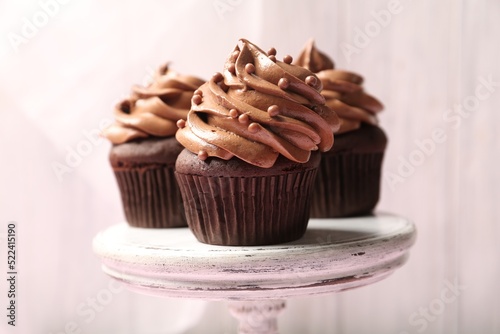 Delicious chocolate cupcakes with cream and beads on white stand, closeup