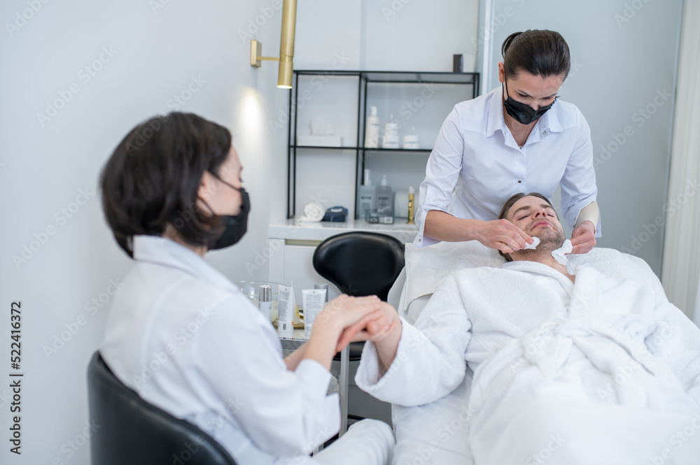 Young man having hand massage and face procedures in the salon Young man having hand massage and face procedures in the salon