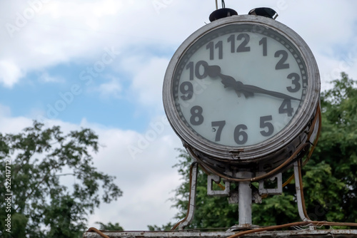 Vintage analog public clock against a blue sky and green trees.