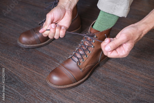 close up of hands of man who tying laces on his fashion brown rough leather boot on wooden background