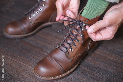 closeup of feet of man in work casual boot and his hands tieds shoelaces on it on wooden floor