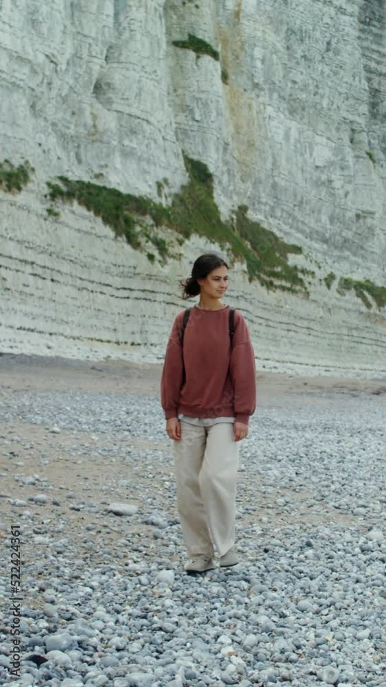 A young woman walks along a pebbly beach past sheer chalk cliffs A young woman walks along a pebbly beach past sheer chalk cliffs