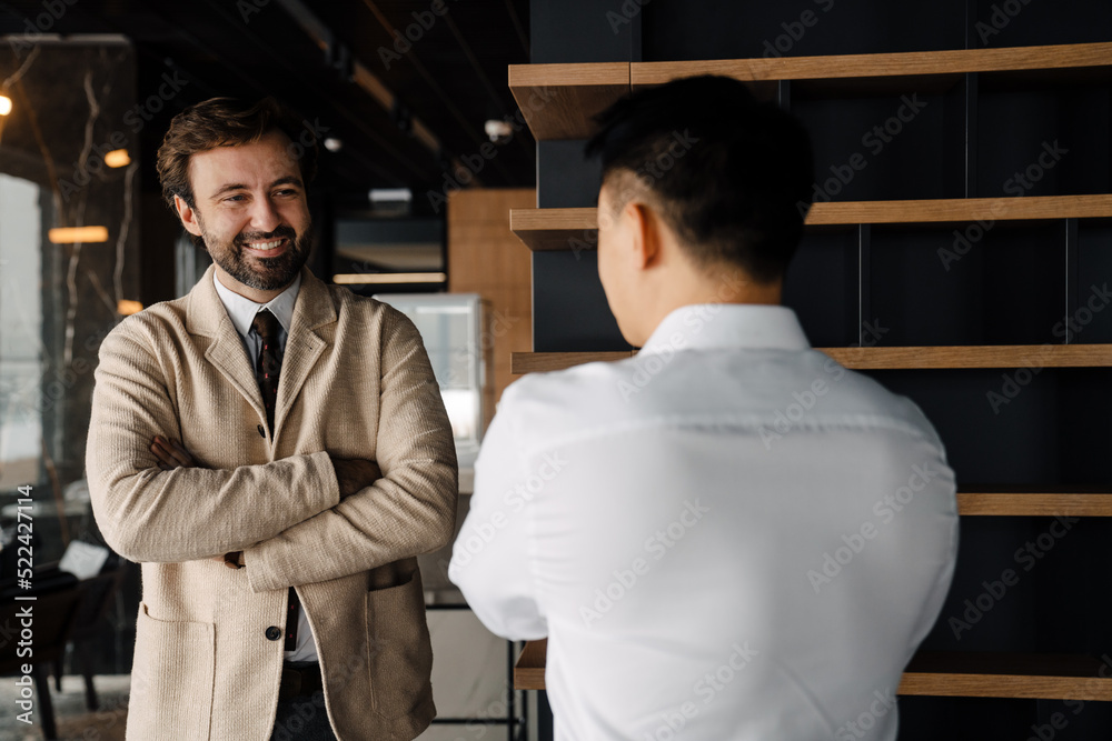 Adult multiracial businessmen smiling and talking in office lobby Adult multiracial businessmen smiling and talking in office lobby