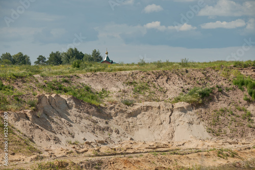 Abandoned sand pit overgrown with grass and cupolas of an Orthodox church in the distance.