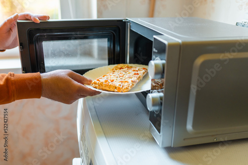 Uncooked frozen small pizza placed into the microwave.junk food,fast food concept.Side view.Selective focus.