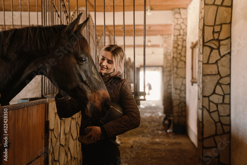 Young blonde jockey woman spending time with her horse