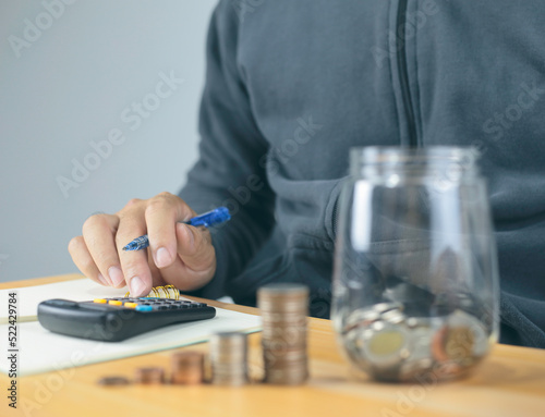 image hand of businessman using calculator and glass bottle saving bank with coins on money stack step. Saving money for future plan, retirement fund. Business investment-finance accounting concept.
