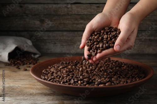 Woman taking pile of roasted coffee beans from bowl at wooden table  closeup