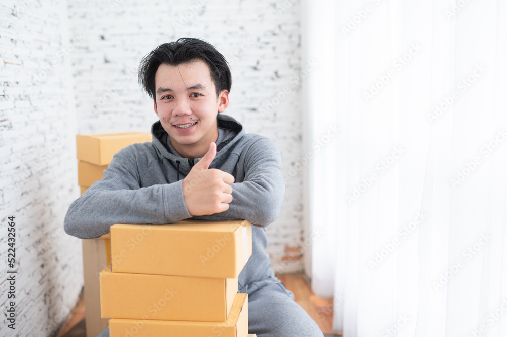A happy young man with boxes showing thumb-up after packing the package delivered to the customer. A happy young man with boxes showing thumb-up after packing the package delivered to the customer.