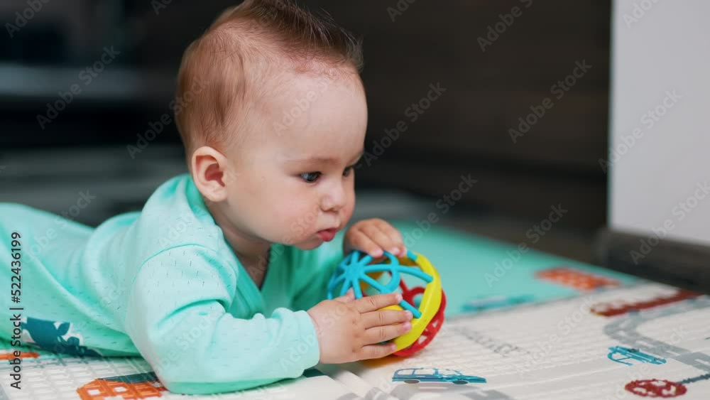 Sweet little baby boy lies on the floor on his belly. Adorable child in blue shirt plays with a bright ball. Close up. Sweet little baby boy lies on the floor on his belly. Adorable child in blue shirt plays with a bright ball. Close up.
