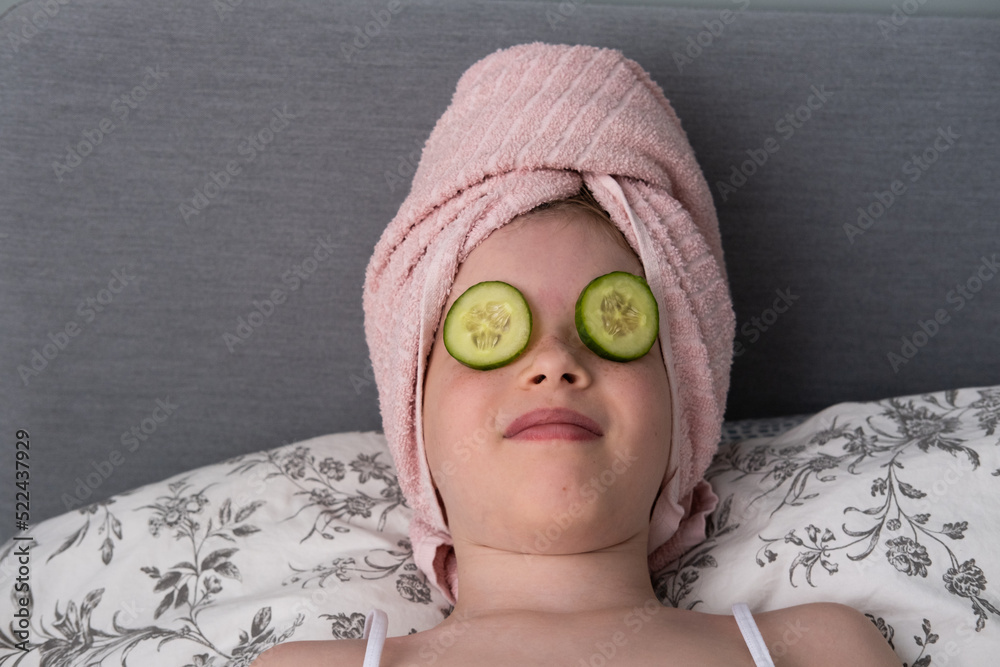 a little beautiful girl is doing spa treatments. Mask with cucumbers on the face