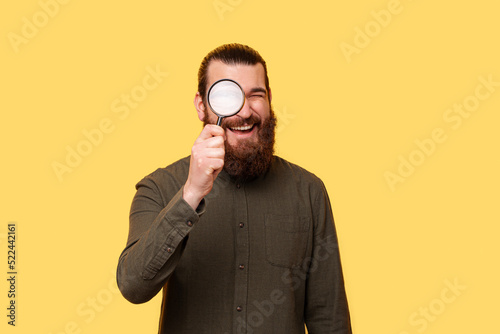 A photo of a young bearded man searching happily with a magnifying glass