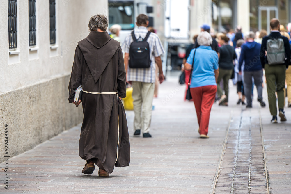 Mönch mit Buch in der Hand zu Fuß in Altstadt unterwegs