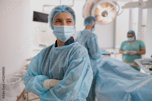 Female surgeon in mask standing in operating room with crossing hands, ready to work on patient photo