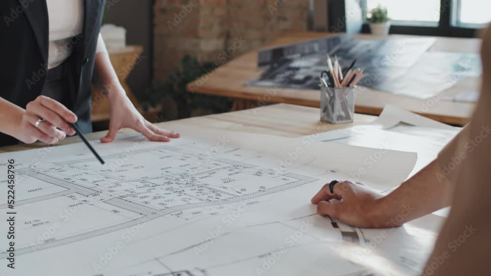 Midsection of two cropped architects discussing floor plan at table in office at daytime