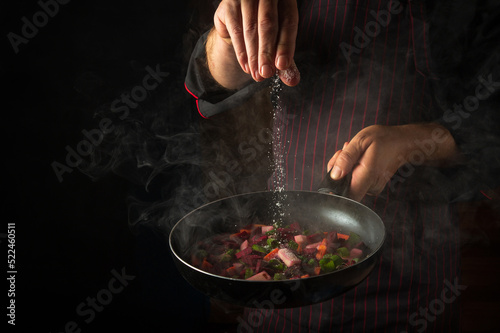 Fototapeta Naklejka Na Ścianę i Meble -  The chef adds salt to a steaming hot pan. Molecular cuisine menu idea for a hotel with advertising space
