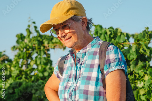 Portrait of caucasian senior woman with yellow cap travelling in Tenerife visiting a vineyard walking amongst grapevines at sunset light.
