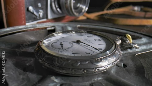 Silver antique pocket watch with rotating hands in time lapse video. An old clock with ticking hands lying on a table next to an old camera. Running clock hands in circle in timelapse. Close up.