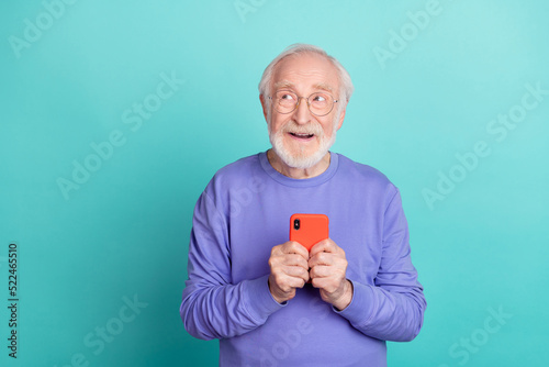 Portrait of minded positive aged man hold telephone look interested empty space isolated on teal color background
