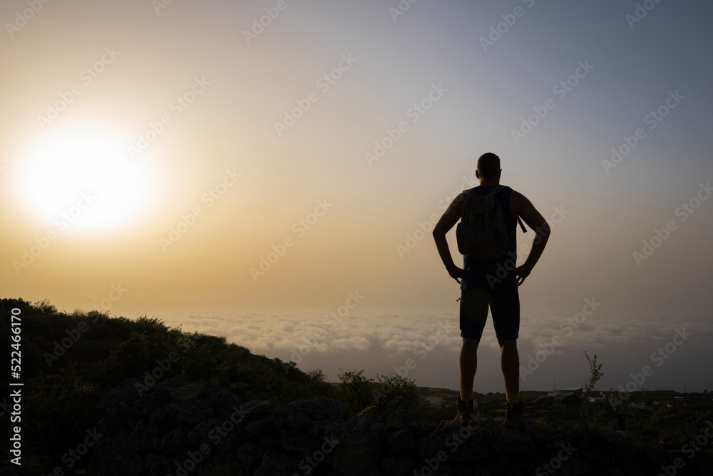 Siluette of tall male hiker on mountain above clouds in sunrise on El Hierro island in summer
