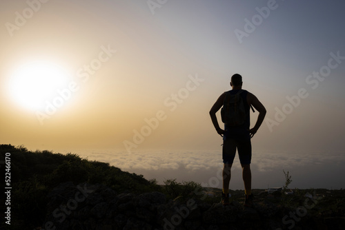 Siluette of tall male hiker on mountain above clouds in sunrise on El Hierro island in summer