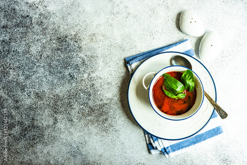 Overhead view of a bowl of gazpacho with bail garnish on a folded napkin with salt and pepper