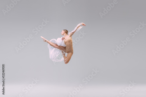 Portrait of young ballerina dancing with fabric isolated over grey studio background. Looks weightless, flexible. Fashion, style.