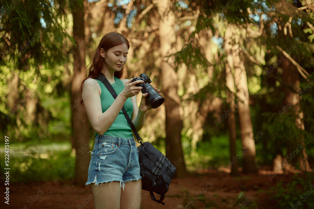 A pretty girl is holding camera in her hands. A young woman in a green top enjoys taking pictures in the forest. A pretty girl is holding camera in her hands. A young woman in a green top enjoys taking pictures in the forest.