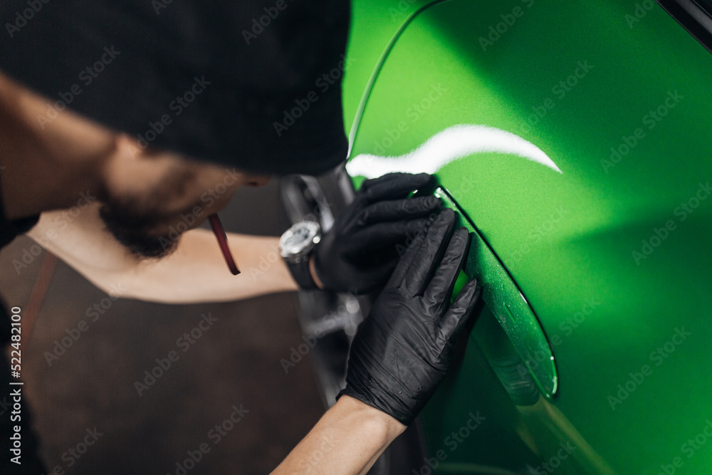 A man makes a detailing of a new car in good lighting, wrapping with a transparent protection film. 