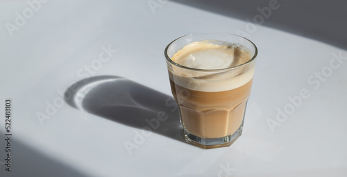 cortado coffee in a glass on a gray background with hard shadows