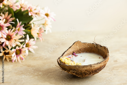 Handmade candle from soy and coconut wax in glass with wooden wick and dry flowers isolated on pastel beige background. Flat lay, top view, copy space