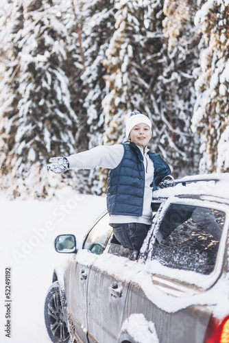 Teenager boy looking out of car window traveling in winter snowy forest. Road trip adventure and local travel concept. Happy child enjoying car ride. Christmas winter holidays and New year vacation