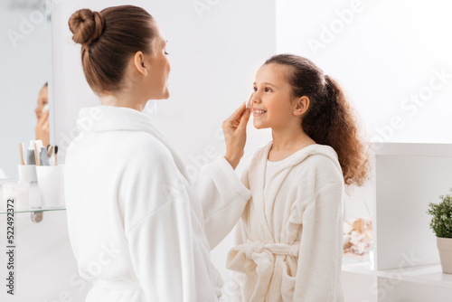 beauty, hygiene, morning and people concept - happy smiling mother with cotton pad cleaning daughter's face skin at bathroom