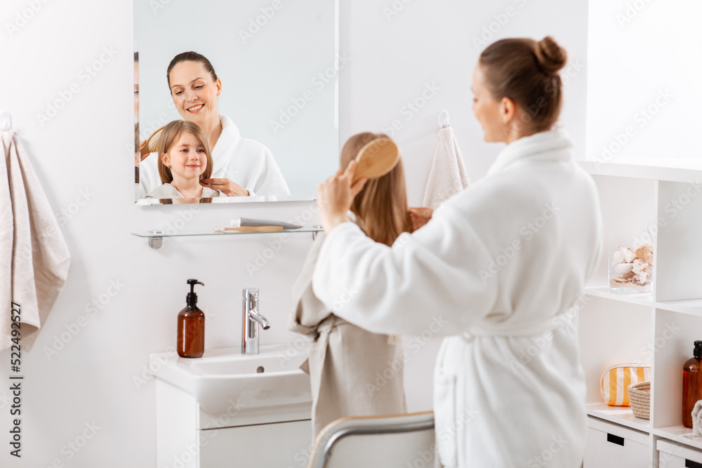 beauty, hygiene, morning and people concept - happy smiling mother and little daughter with hairbrush brushing hair at bathroom