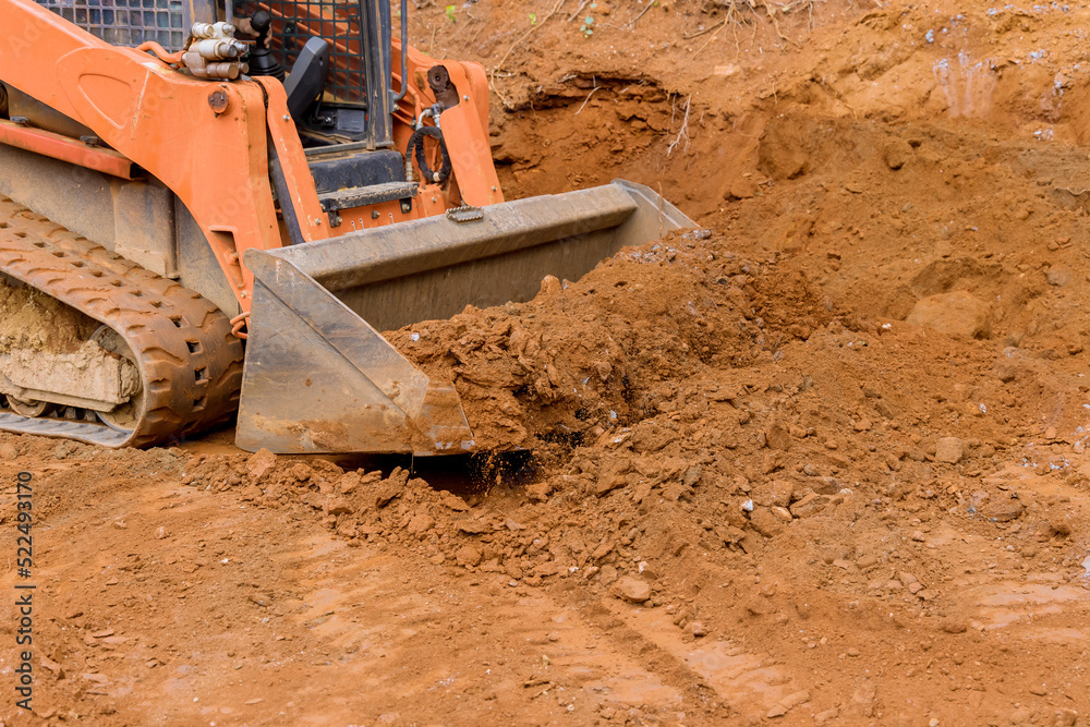 There is a small tractor working with the earth moving equipment for leveling land near new house. There is a small tractor working with the earth moving equipment for leveling land near new house.