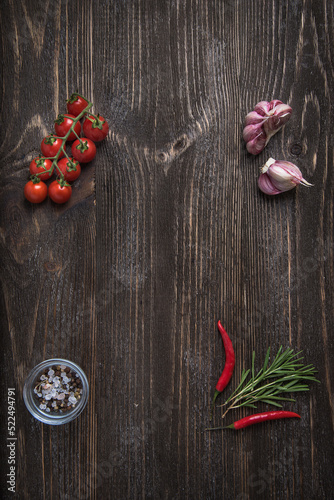 Wooden background with vegetable decor: cherry tomatoes, garlic, rosemary and chilli peppers