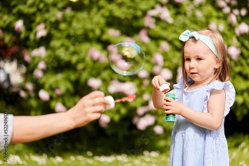 childhood, leisure and people concept - happy little girl blowing soap bubbles at summer park or garden