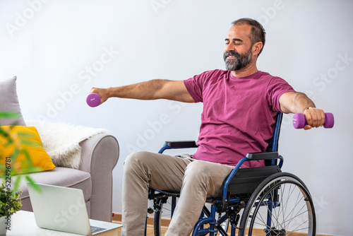 Rehabilitation workout of paraplegic people. Millennial man in wheelchair training with dumbbells at home. Disabled mature guy doing domestic physiotherapy exercises © Dragana Gordic