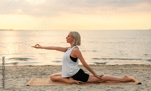 fitness  sport  and healthy lifestyle concept - woman doing yoga pigeon pose on beach over sunset