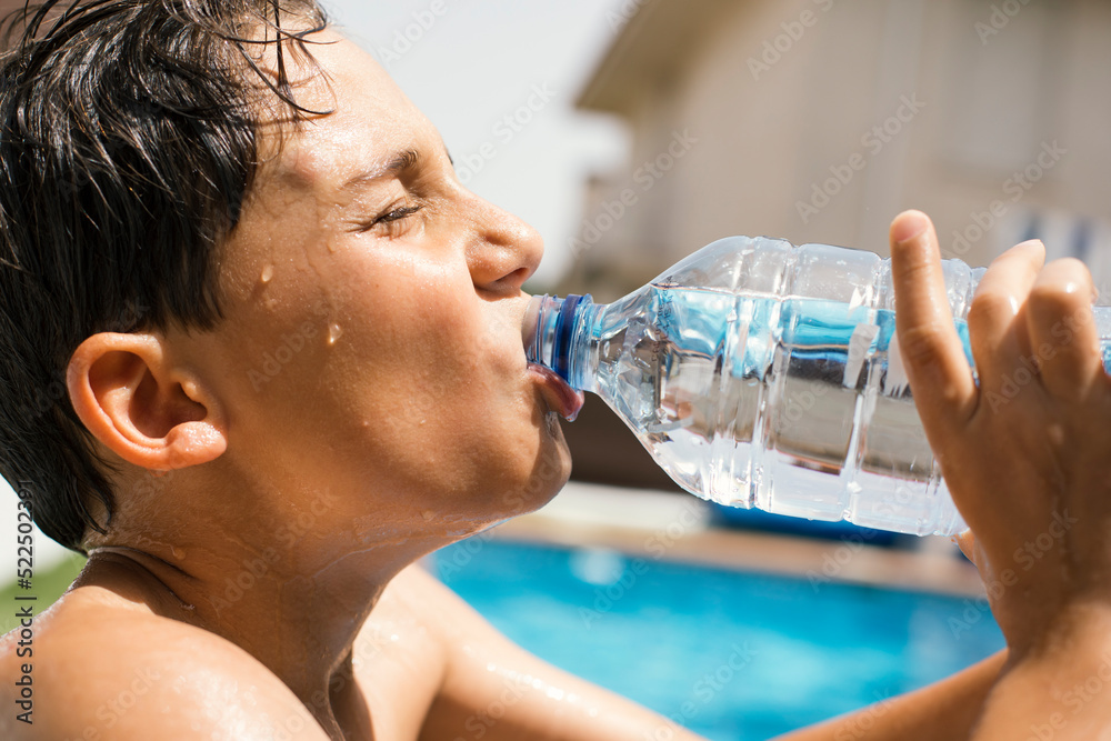 Fotografia do Stock Boy drinking water from a plastic bottle under a