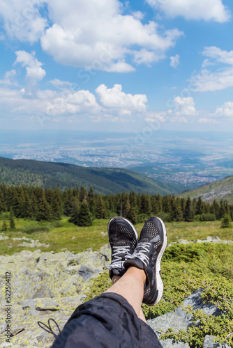 Legs of Traveler Woman Sitting on a High Mountain Top with City View.